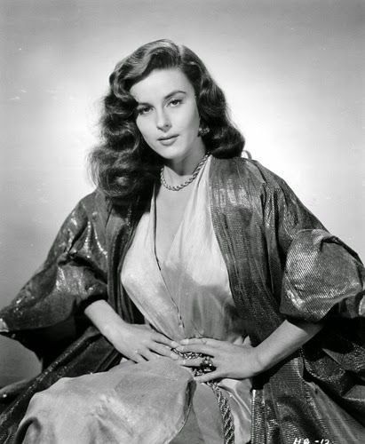 a black and white photo of a woman with long hair sitting on a chair wearing a dress