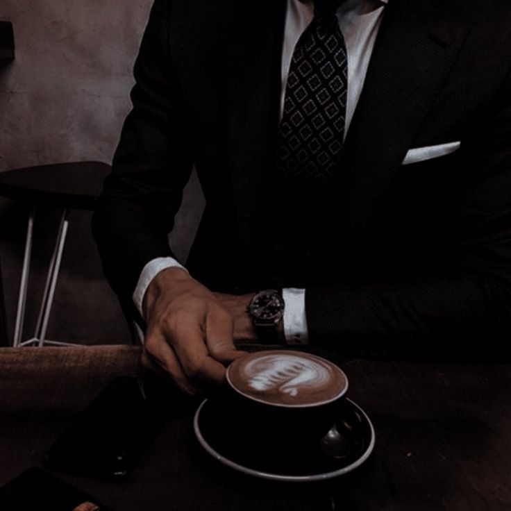 a man in a suit sitting at a table with a cappuccino