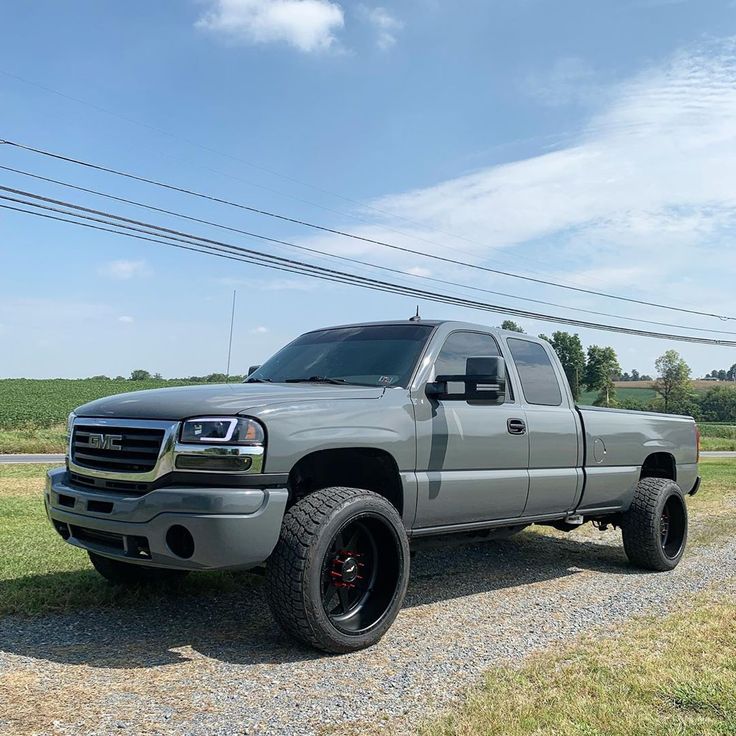 a silver truck parked on top of a gravel road next to a green grass covered field