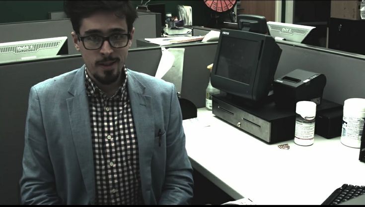 a man wearing glasses sitting in front of a desk with a computer monitor and keyboard