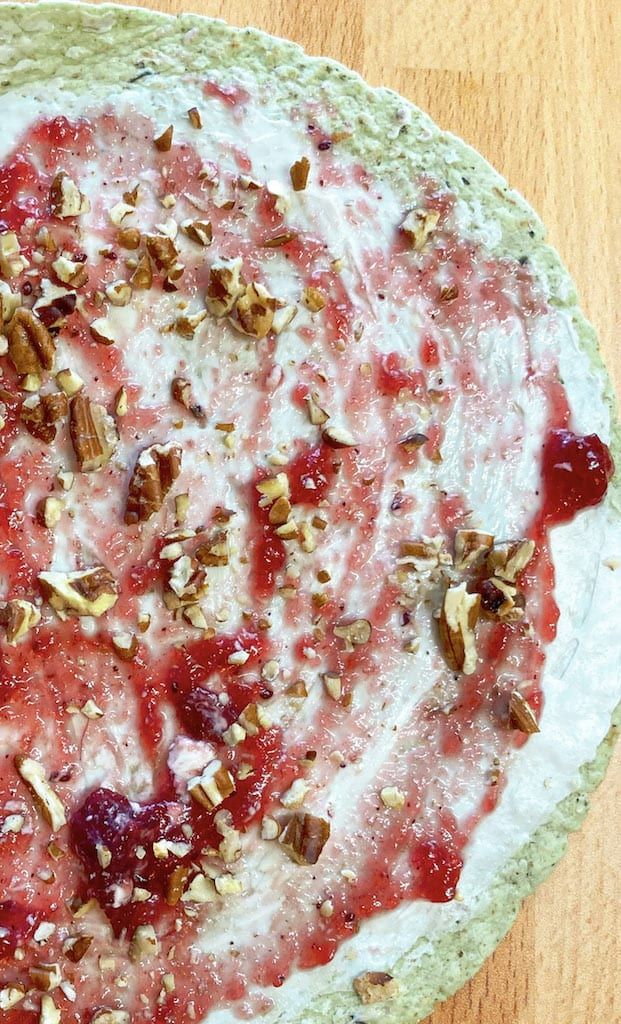 an uncooked pizza with cranberry sauce and pecans