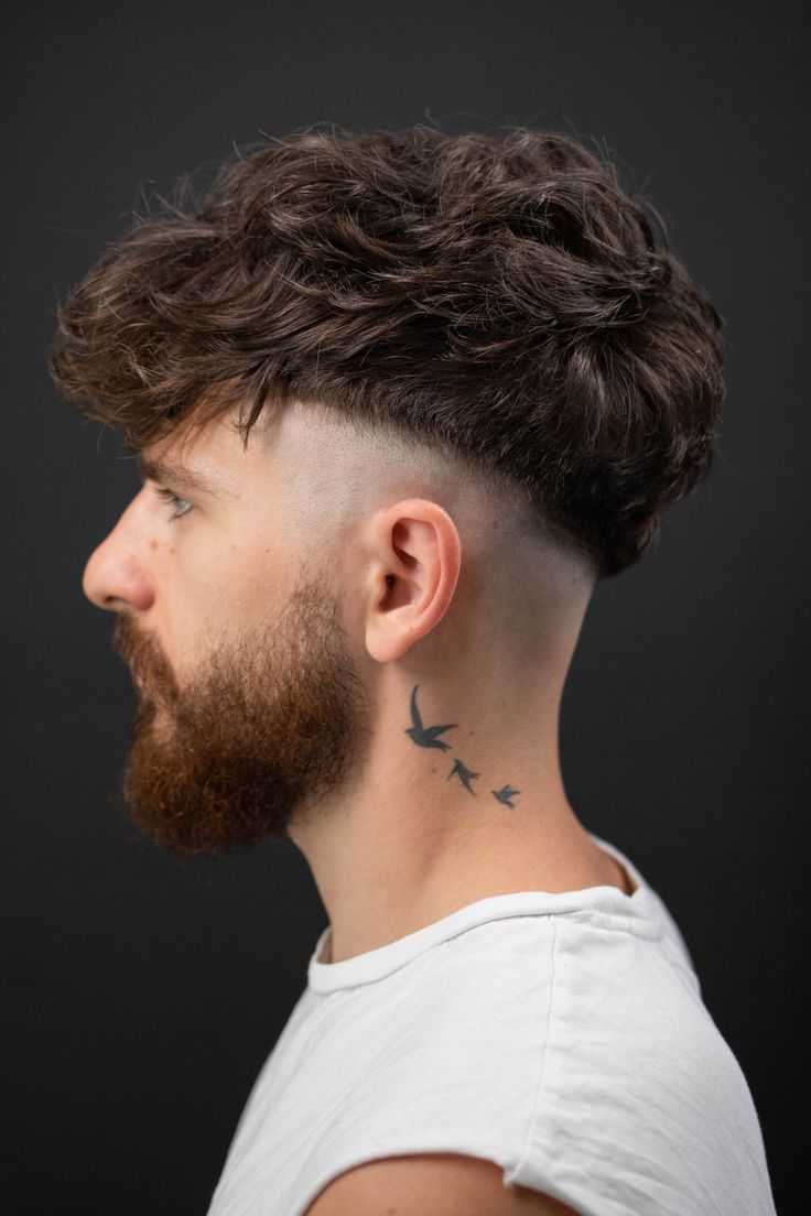 a man with a bird tattoo on his neck looking to the side, against a black background