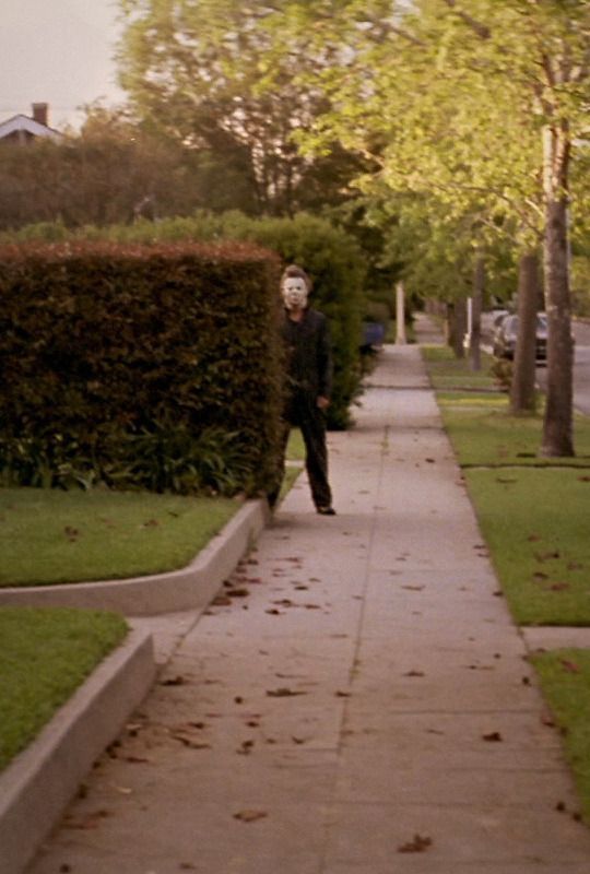 a man walking down a sidewalk next to a lush green park