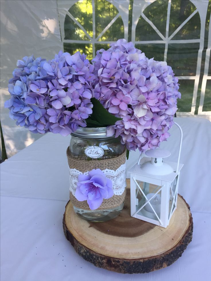 purple flowers are in a mason jar on top of a wood slice with a lantern