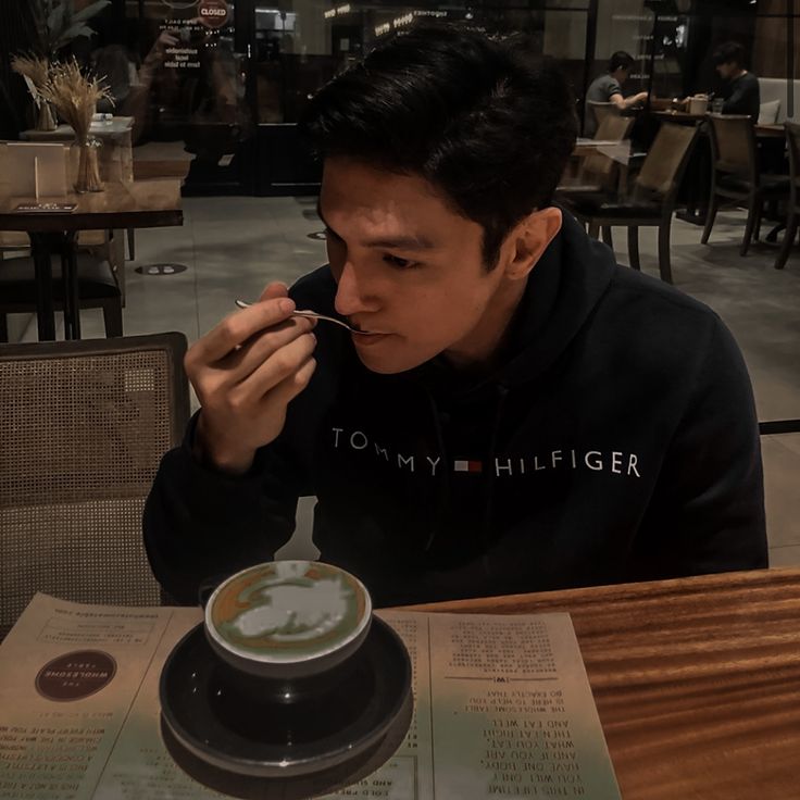 a man sitting at a table eating food from a bowl with chopsticks in his mouth