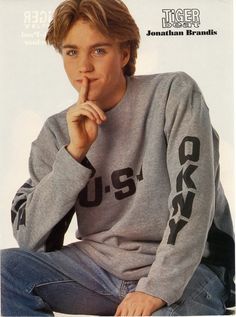 a young man sitting on the ground with his finger in his mouth and looking at the camera