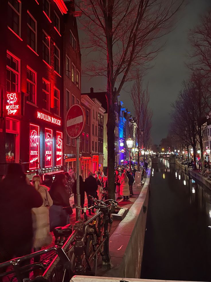 people are walking down the street at night with neon lights on buildings in the background