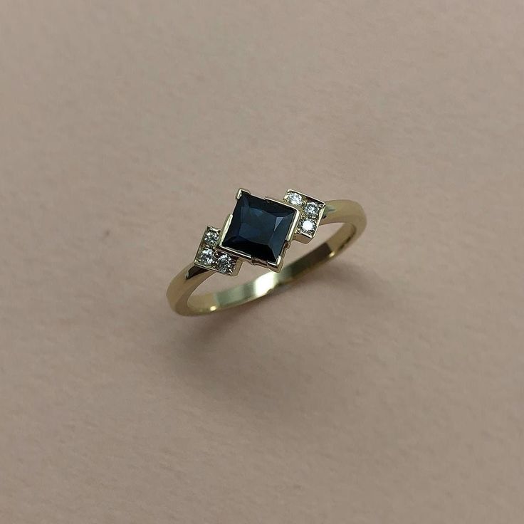 a gold ring with a black diamond and two diamonds on the side, sitting on a beige surface