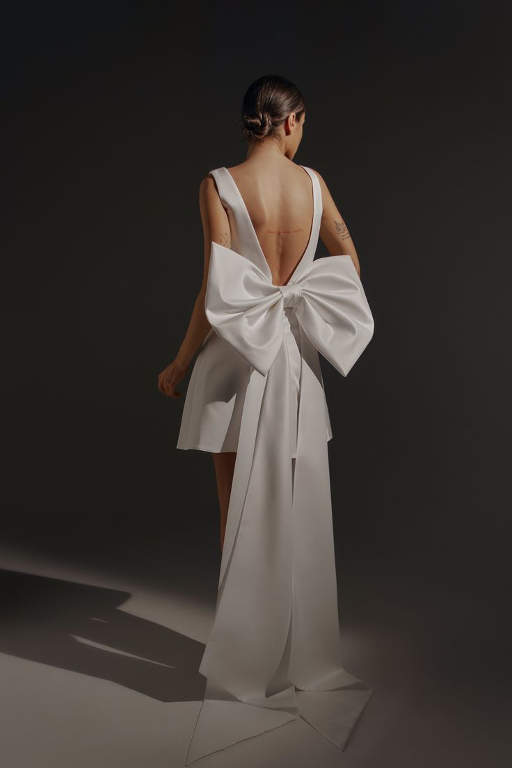 the back of a woman's white dress with a large bow on her shoulder