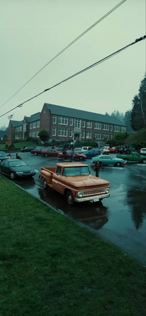 an old red truck is parked in the parking lot on a rainy day with other cars