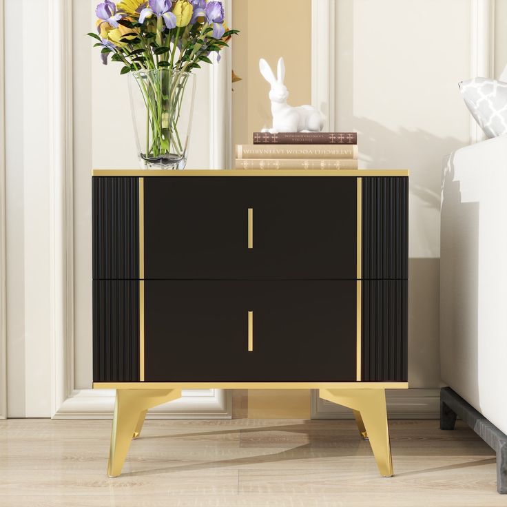 a black and gold sideboard with flowers in a vase next to it on top of a hard wood floor