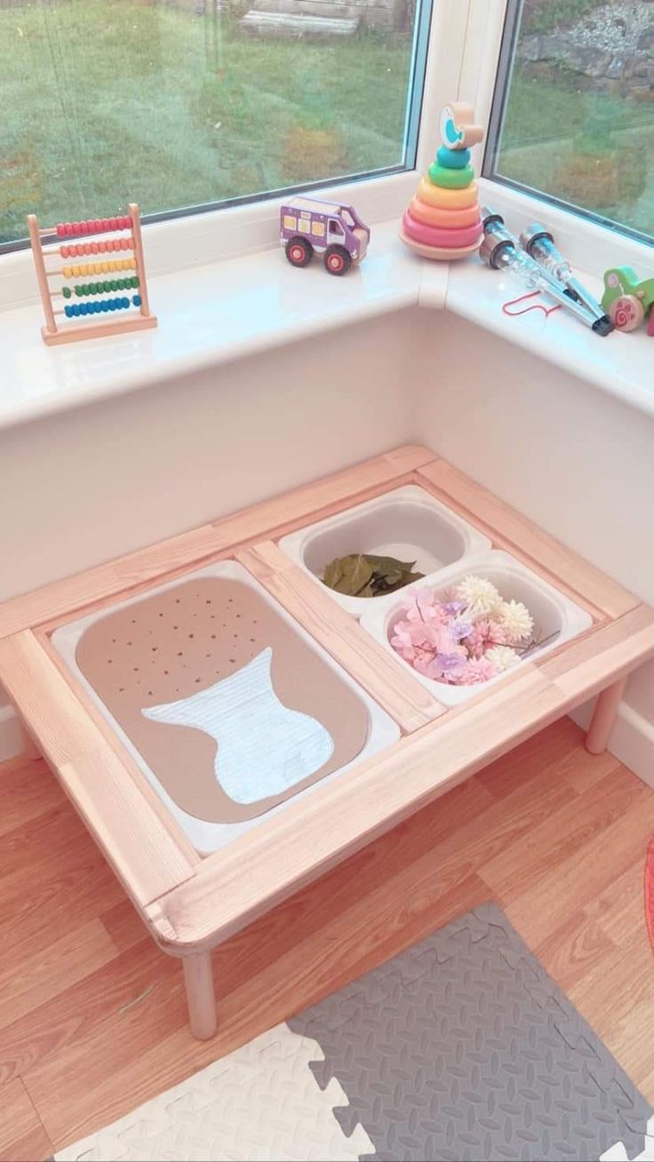 a child's play table with two trays and toys on the window sill