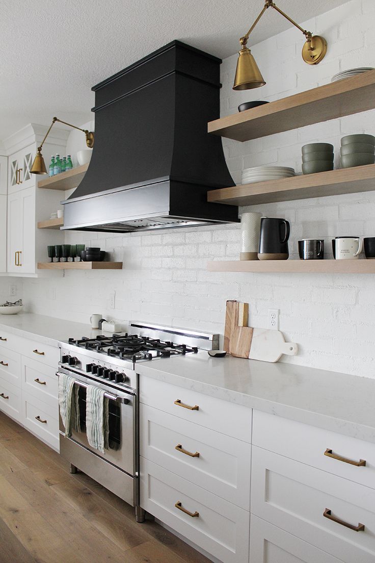 a stove top oven sitting inside of a kitchen next to white cabinets and wooden shelves