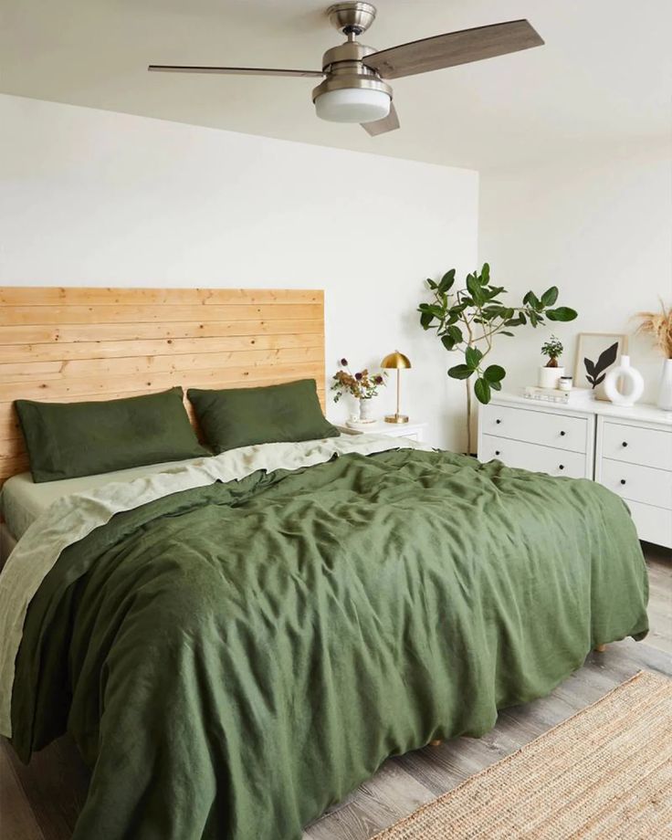 a bed with green sheets and pillows in a bedroom next to a ceiling fan on the wall