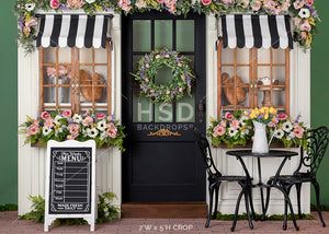 two chairs and a table in front of a green building with flowers on the windows