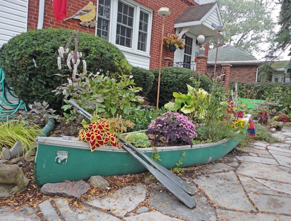 a boat filled with lots of plants sitting on top of a stone floor next to a house