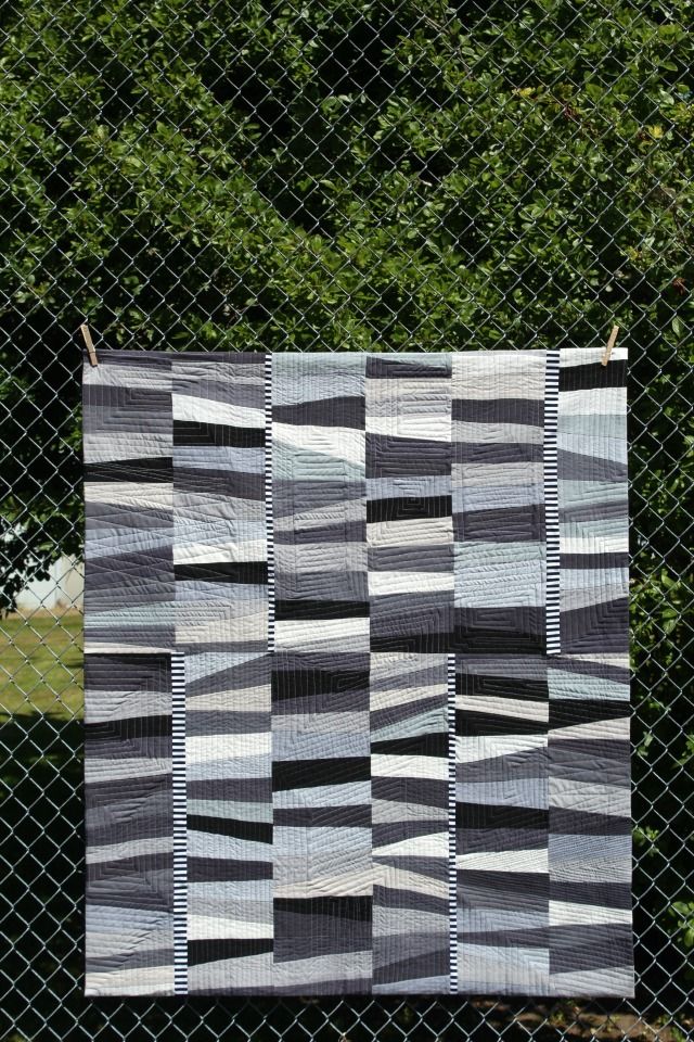 a black and white quilt hanging on a chain link fence with trees in the background