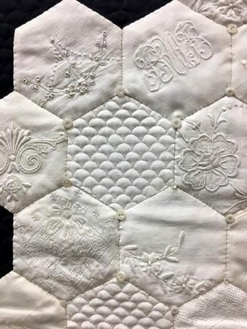 an embroidered hexagonal quilt with white threadwork on the edges and appliques