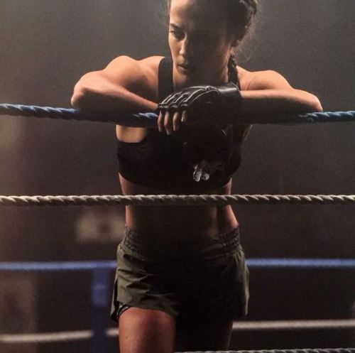 a woman standing on top of a wrestling ring holding a pair of gloves over her shoulder