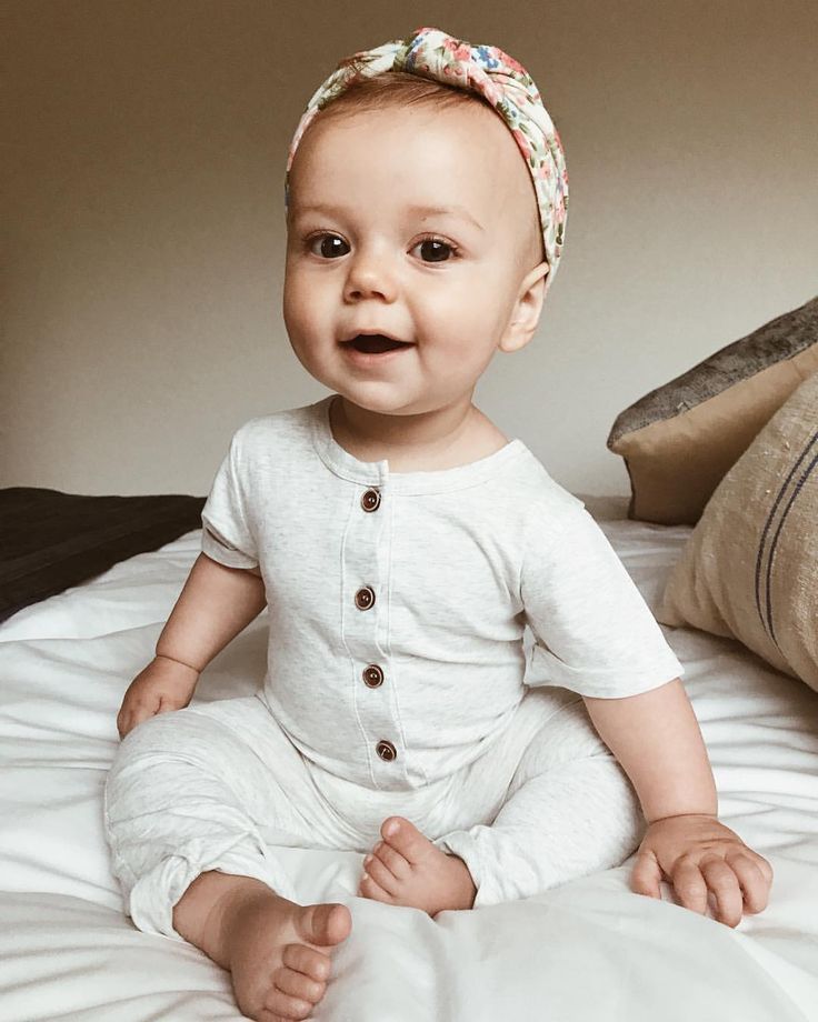 a baby sitting on top of a bed next to pillows and pillow cases, with a surprised look on its face