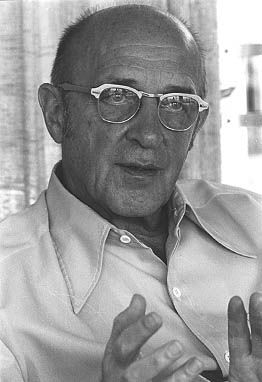 black and white photo of an older man with glasses pointing at something in front of him