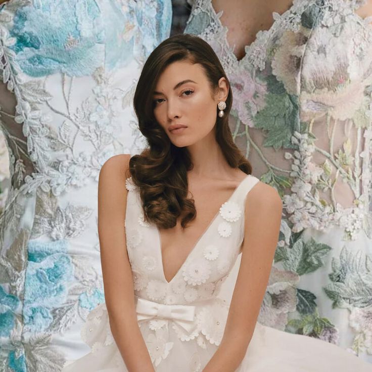 a woman in a white dress sitting next to two dresses with flowers on the back