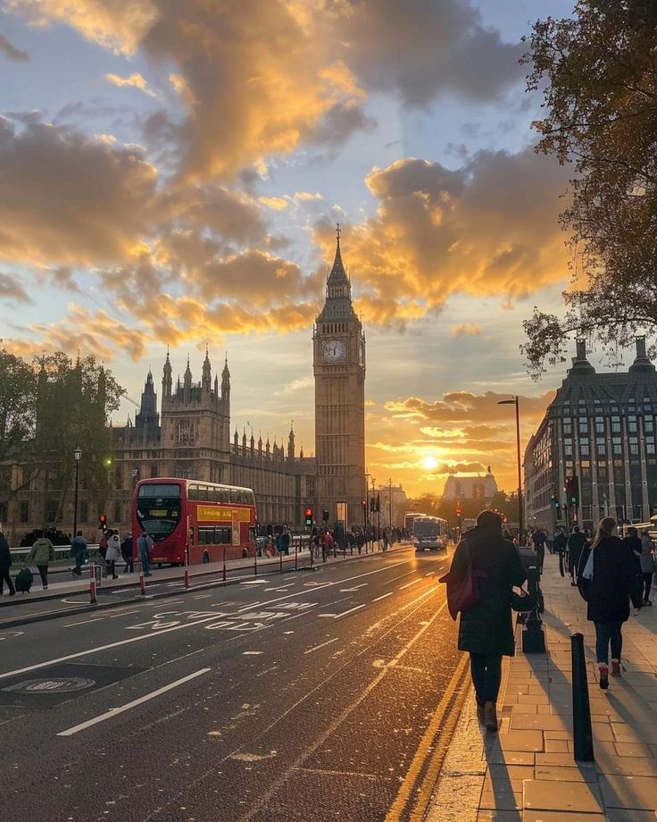 the sun is setting over big ben in london, england as people walk down the street