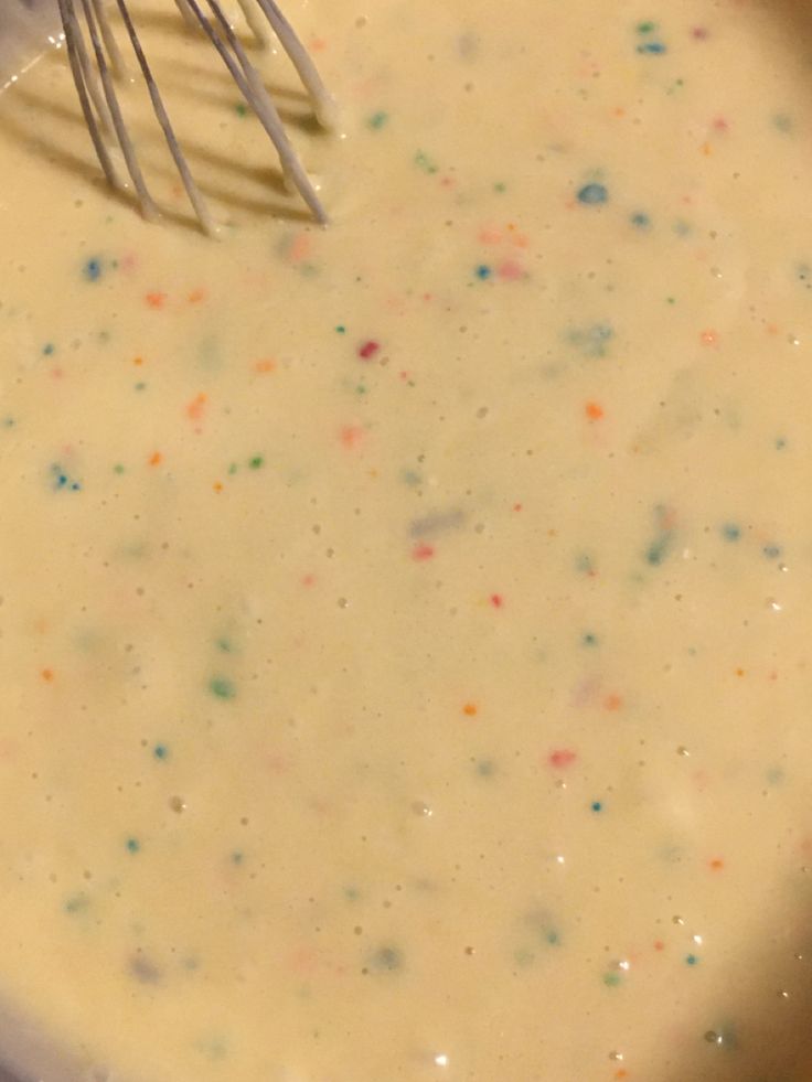 a whisk in a bowl filled with batter and sprinkles