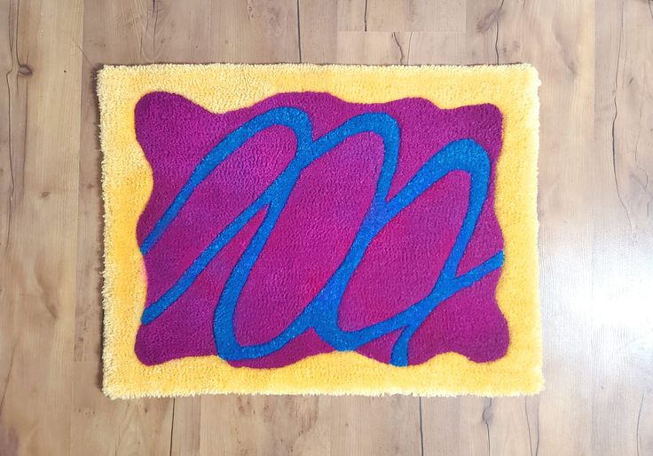 a purple and yellow area rug with blue letters on the bottom right corner, in front of a wood floor