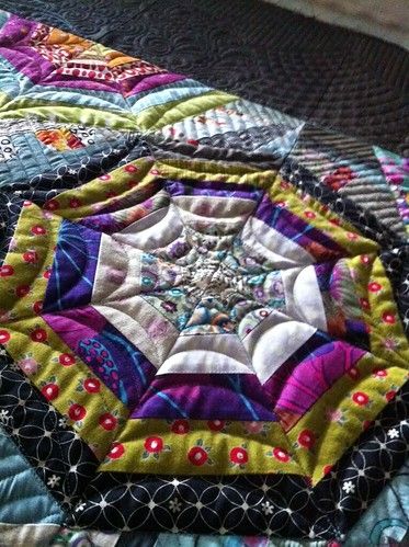 a close up of a quilt on a bed with many different colors and shapes in it