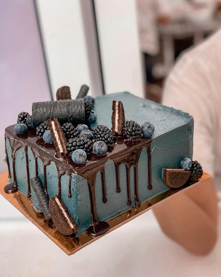 a blue cake with chocolate icing and berries on top is being held by a woman