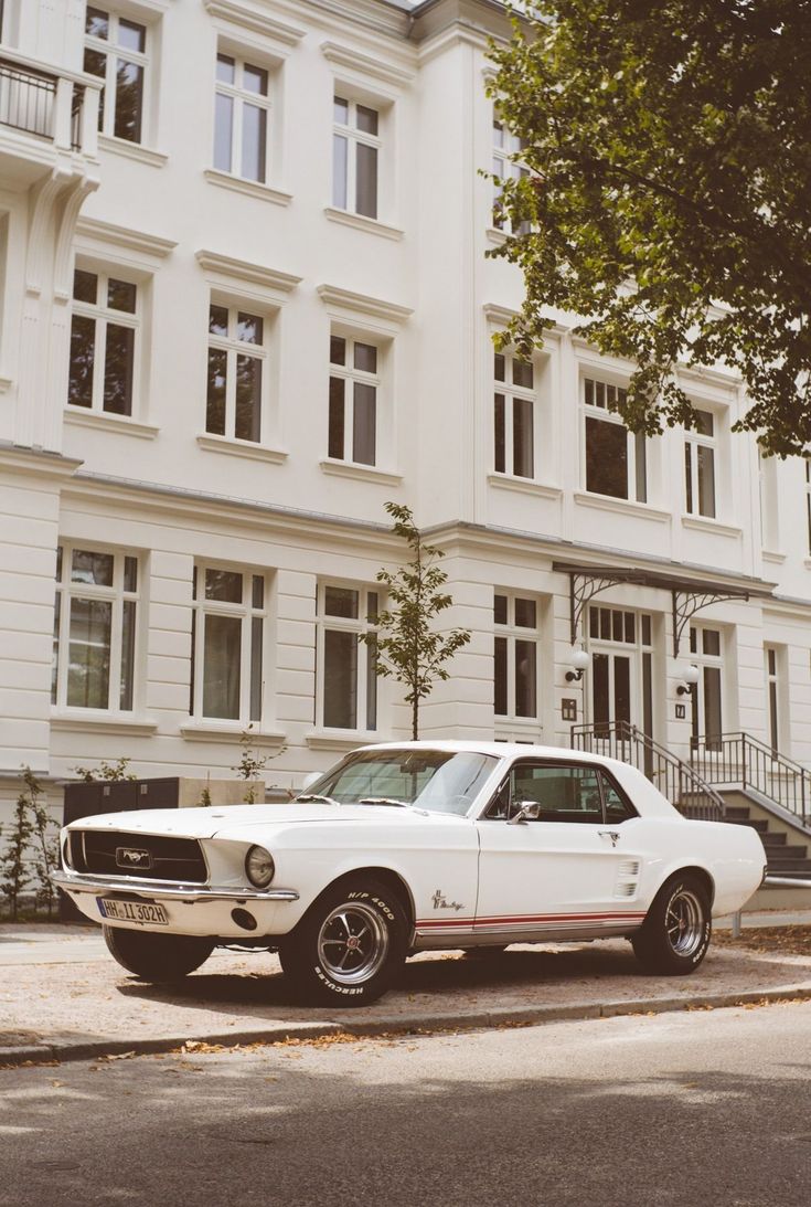 an old car parked in front of a large white building