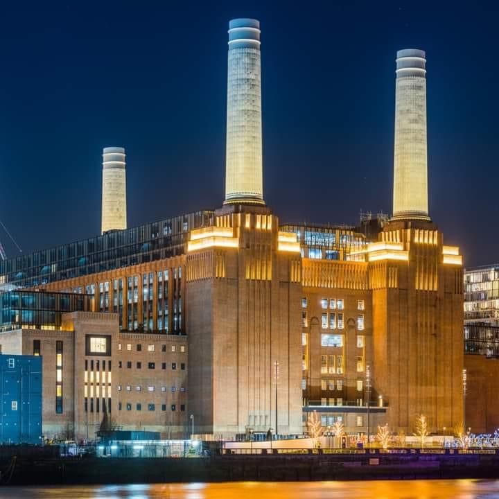 an industrial building lit up at night with the lights on and buildings in the background