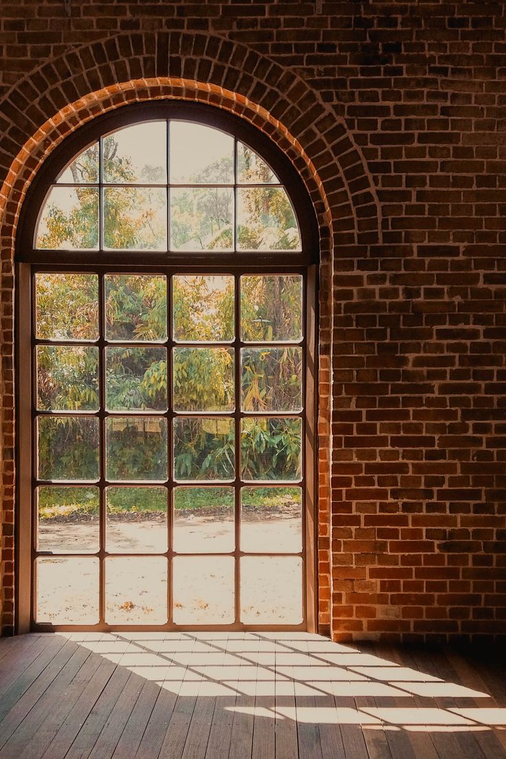 an open window in a brick wall with wood flooring and sunlight streaming through it