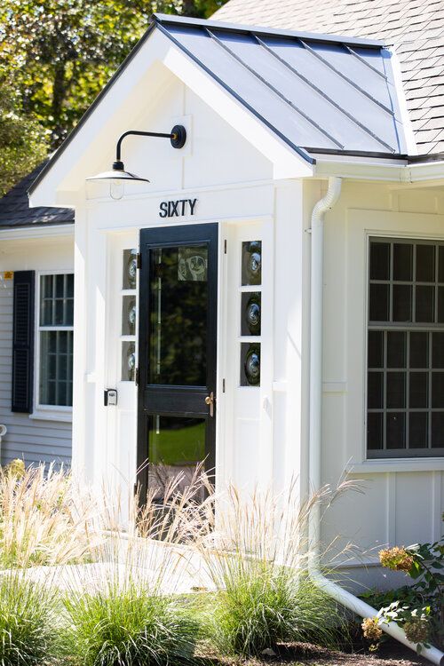 a small white building with a black door and window on the front, surrounded by tall grass