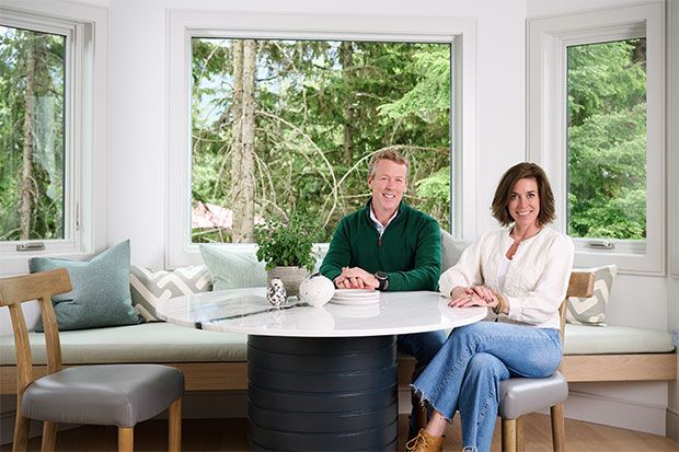 a man and woman sitting at a table in front of two large windows, smiling for the camera