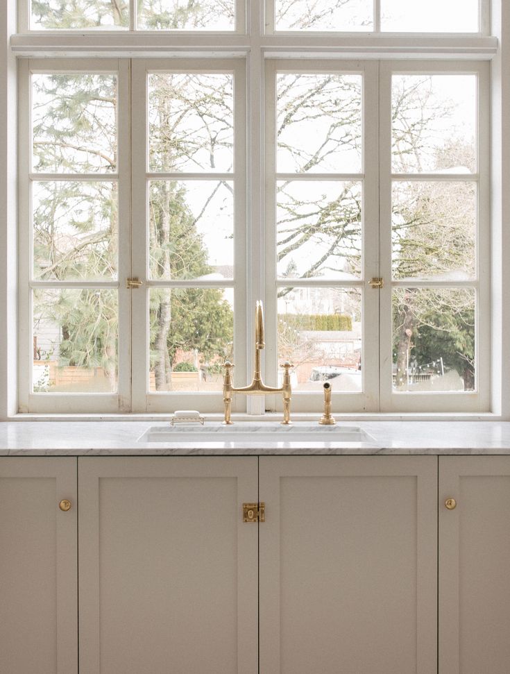 a kitchen sink sitting under a window next to a white counter top with gold faucets