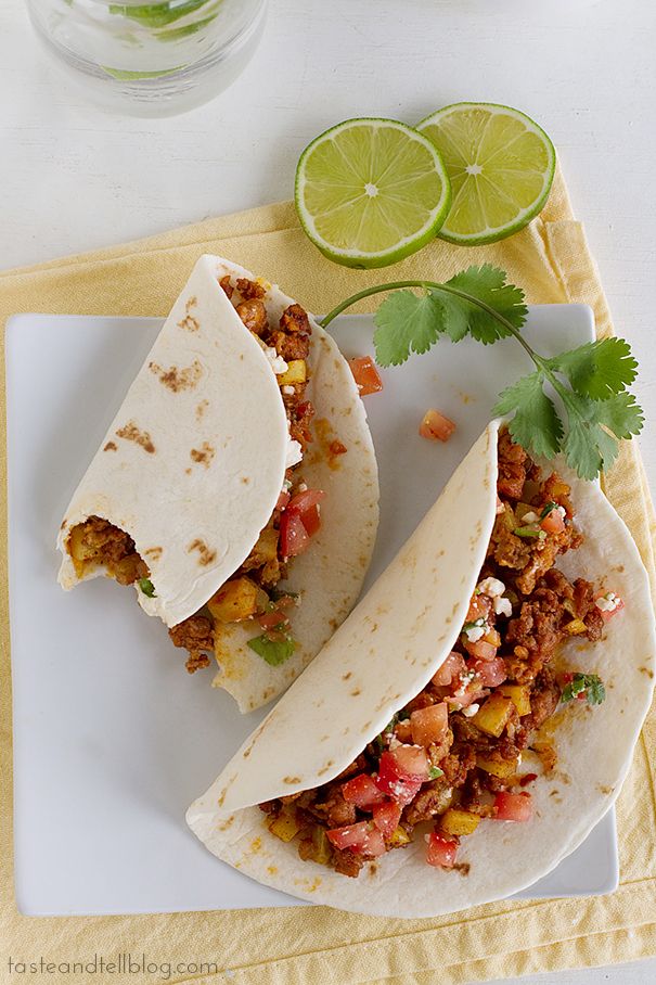 two tacos on a plate with limes and cilantro