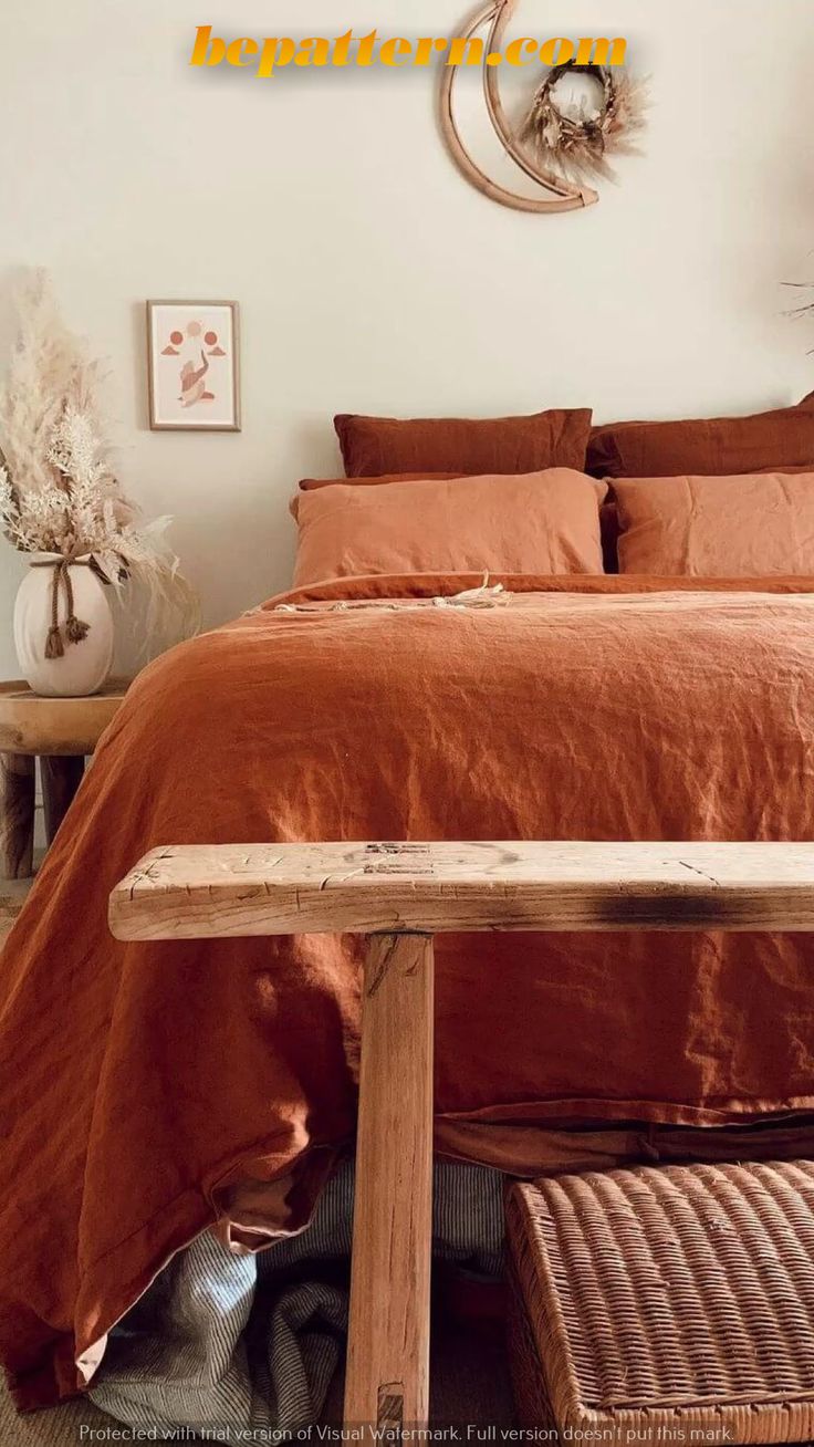 a bed with an orange comforter on top of it next to a wooden bench