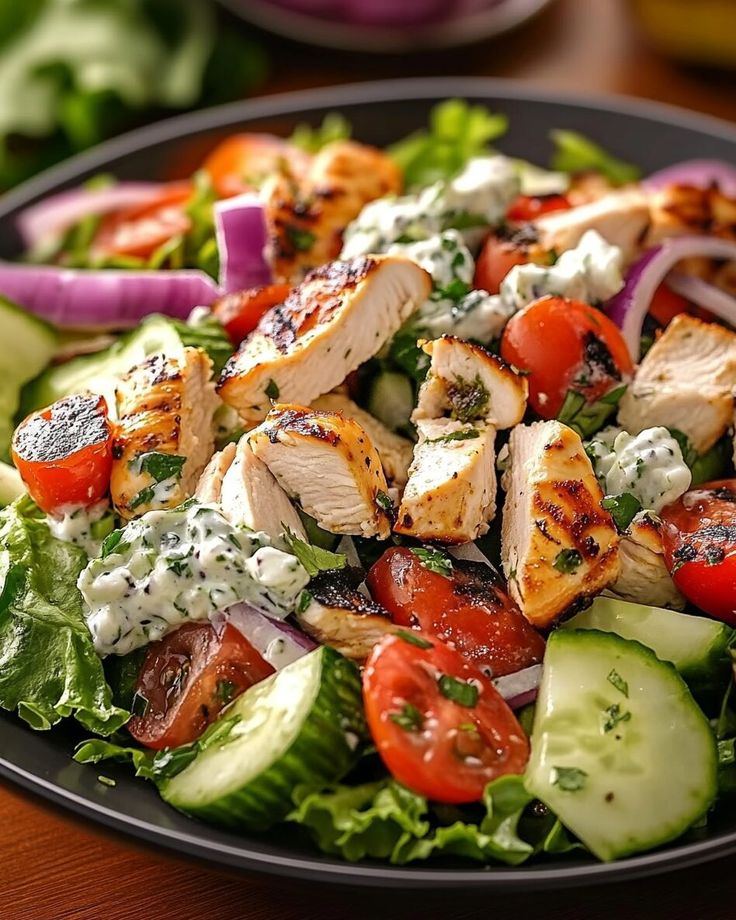 a salad with chicken, tomatoes, cucumbers and dressing on it is sitting on a table