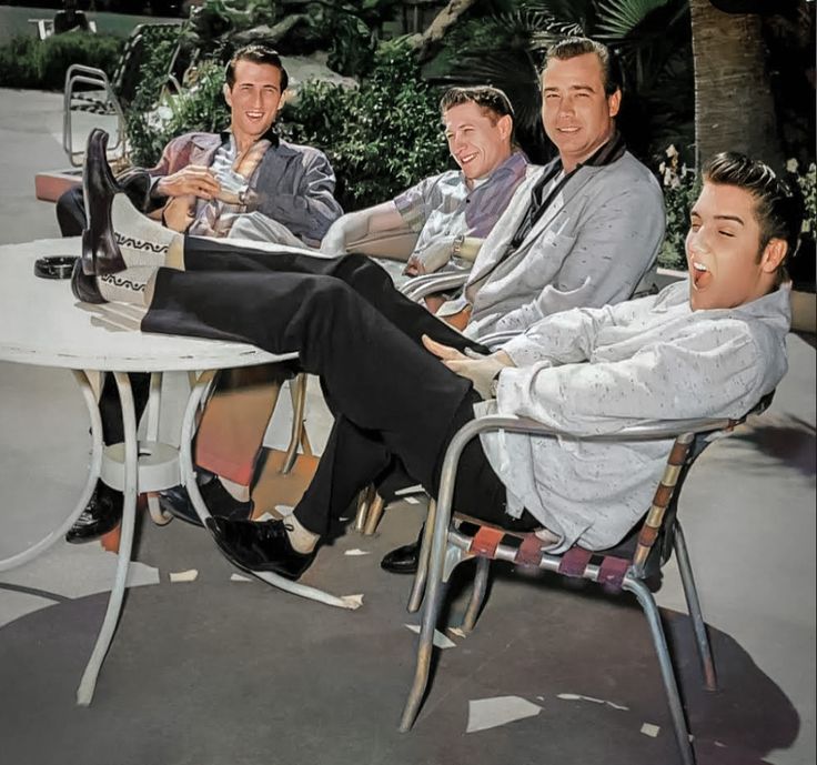 four men sitting at a table with wine bottles in their hands and one man holding a bottle