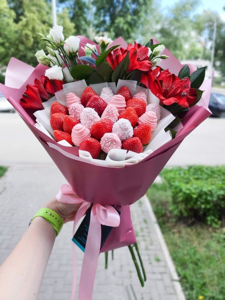 a person holding a bouquet of flowers and strawberries in their hand on the sidewalk