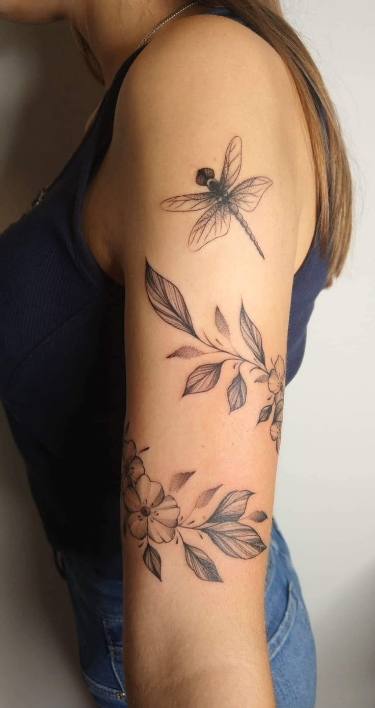 a woman's arm with flowers and dragonfly tattoo on the back of her arm