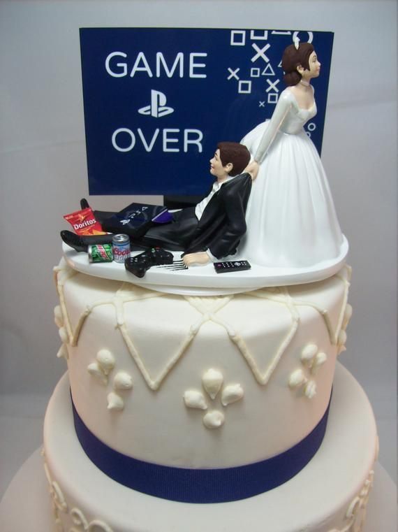 a wedding cake with a bride and groom on top, sitting in front of a game over sign