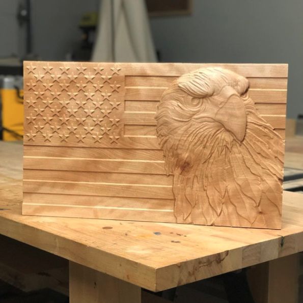 an eagle head carved into the side of a wooden american flag plaque on a workbench