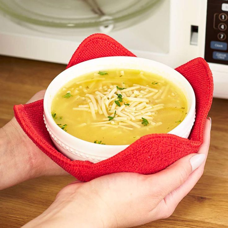 a person holding a bowl of soup in front of a microwave