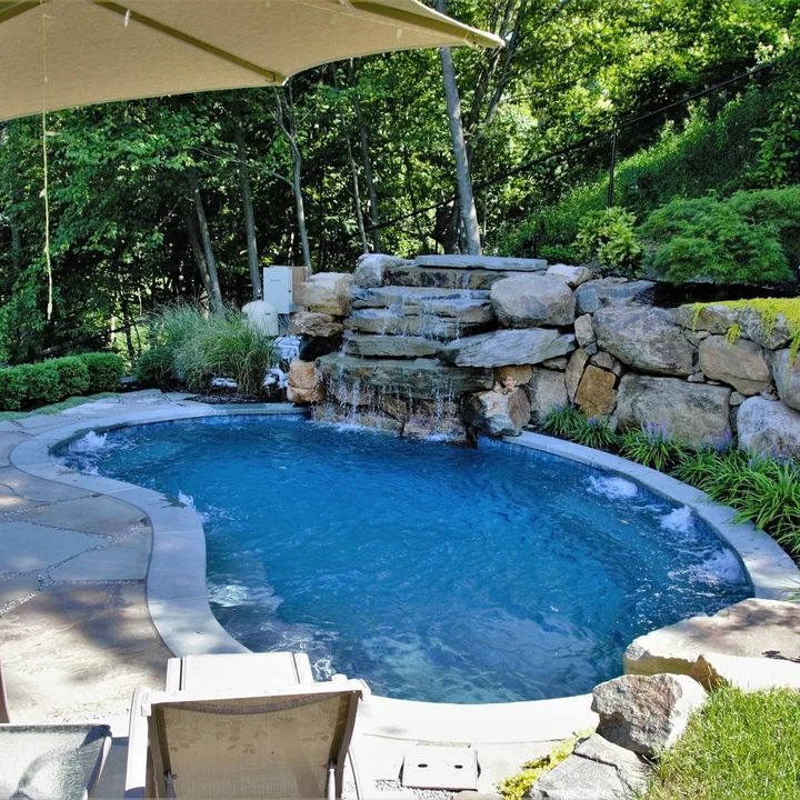 an outdoor pool surrounded by rocks and water features a waterfall that flows into the pond