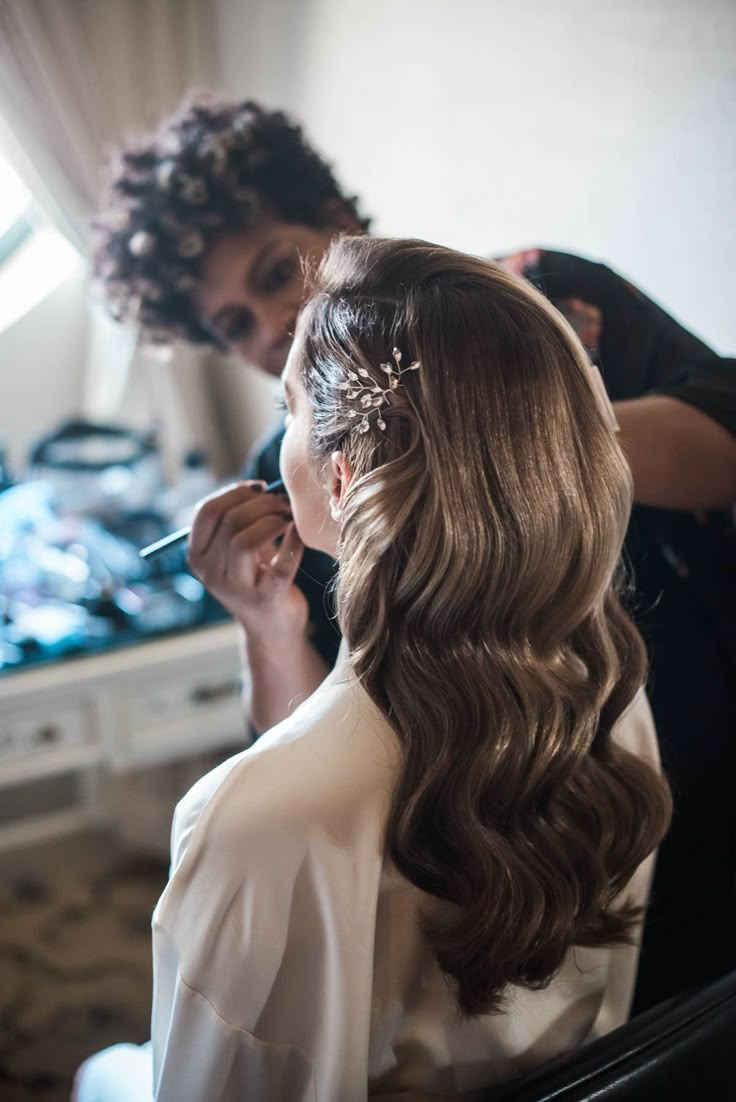 a woman is getting her hair done while another person looks on in the mirror behind her