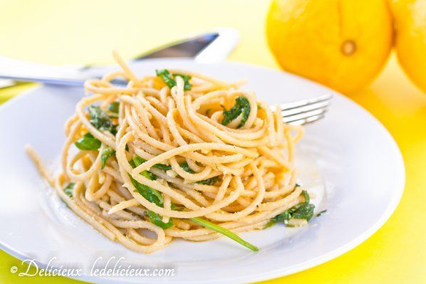 a white plate topped with pasta next to two lemons and a fork on a yellow table