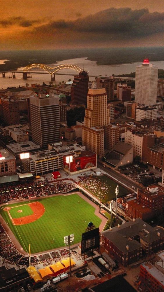 an aerial view of a baseball field in the middle of a city at sunset or dawn